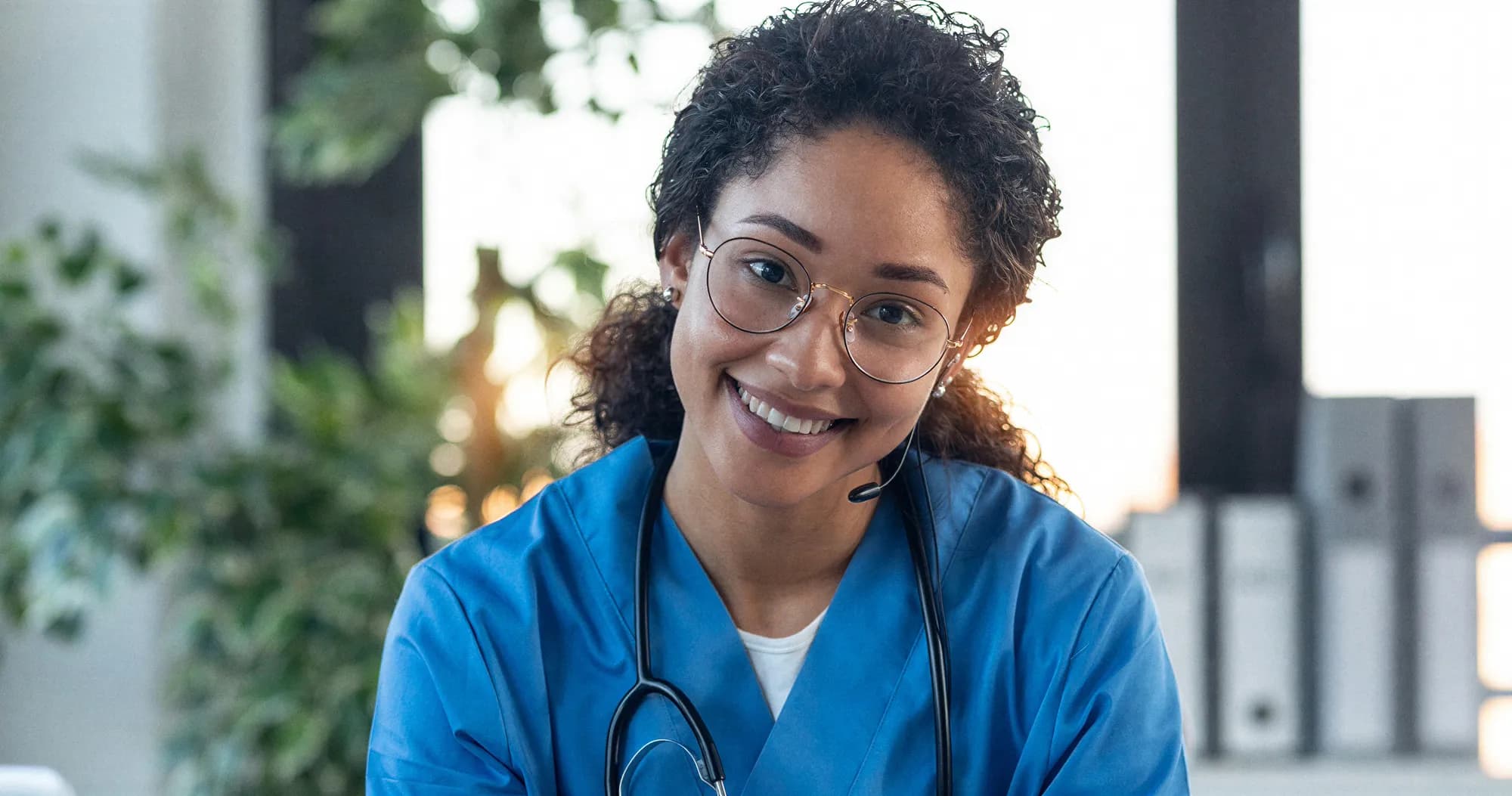 Smiling clinician in scrubs wearing a headset and stethoscope